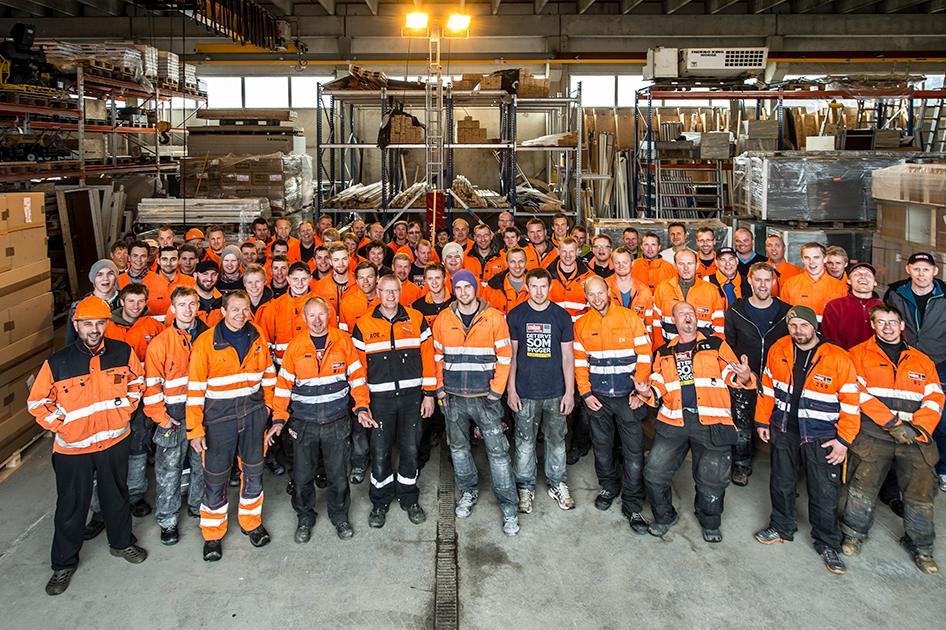 MBA-gjengen, de fleste i oransje arbeidsklær, samlet til gruppebilde i en lagerhall